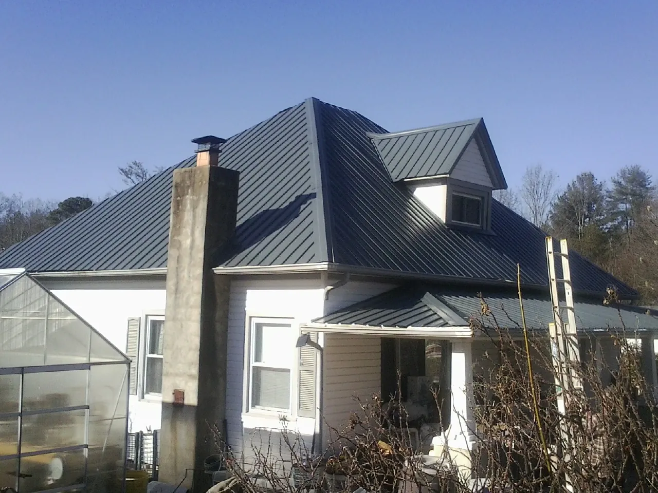 Dark blue standing seam metal roof on a white farmhouse with dormer — Slate & Tile Roof Repair by Roofing Brothers in Versailles