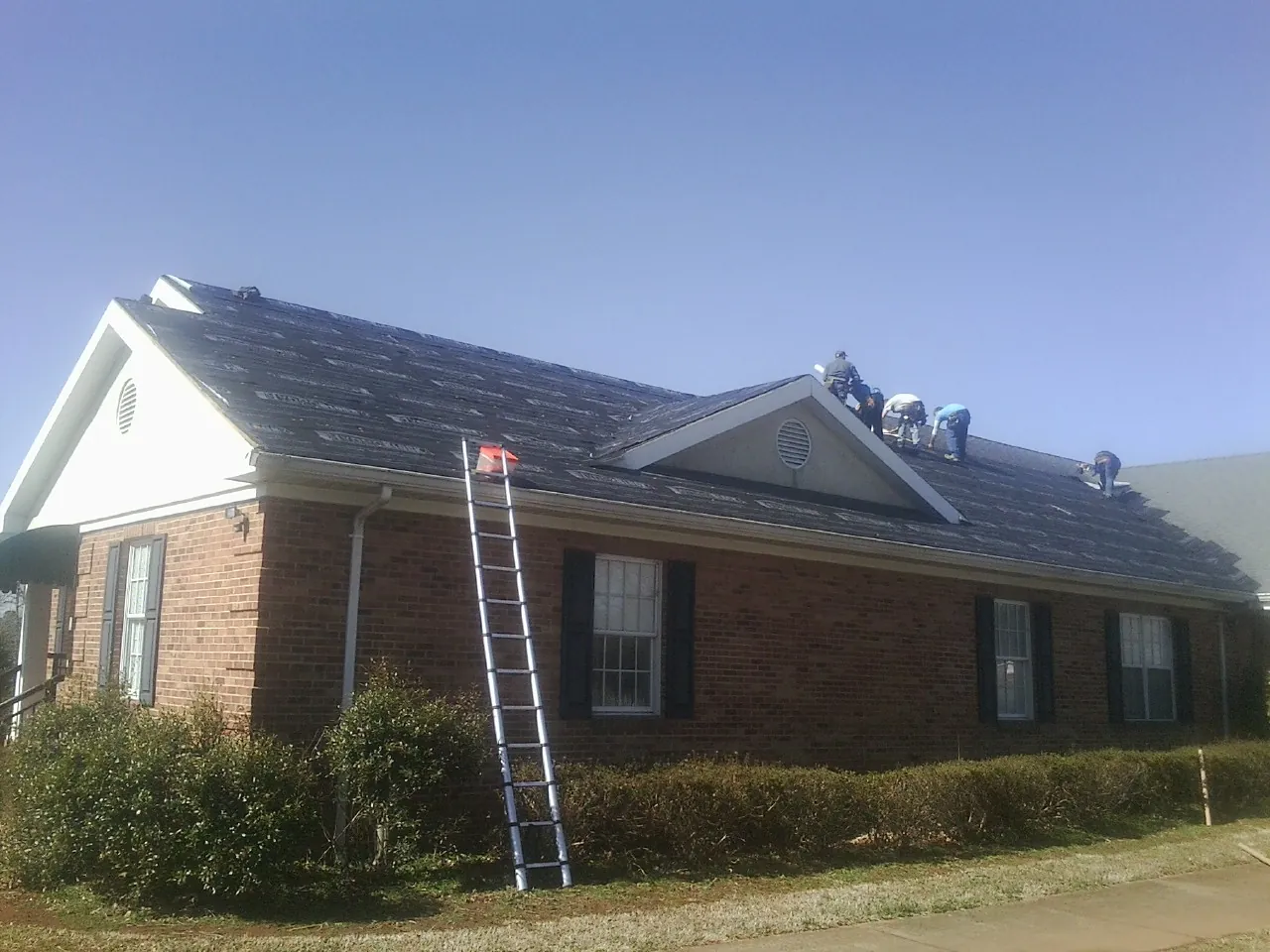 Crew tearing shingles off a brick ranch roof with a ladder set — Metal Roof Repair work by our crew in Versailles
