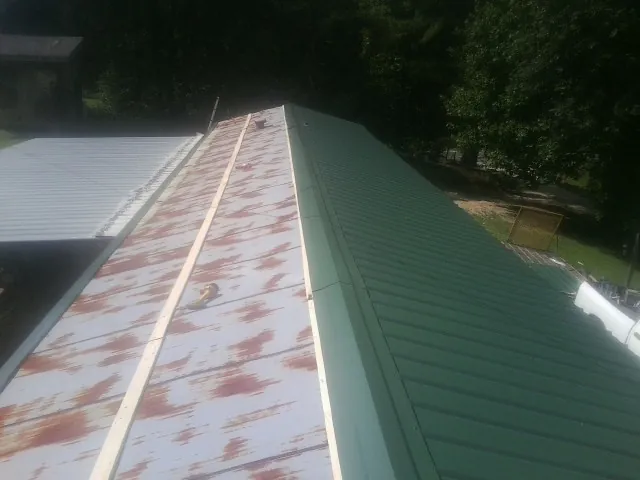 Old rusted panels beside newly installed green metal roofing — Wind Damage Roof Repair by Roofing Brothers in Versailles