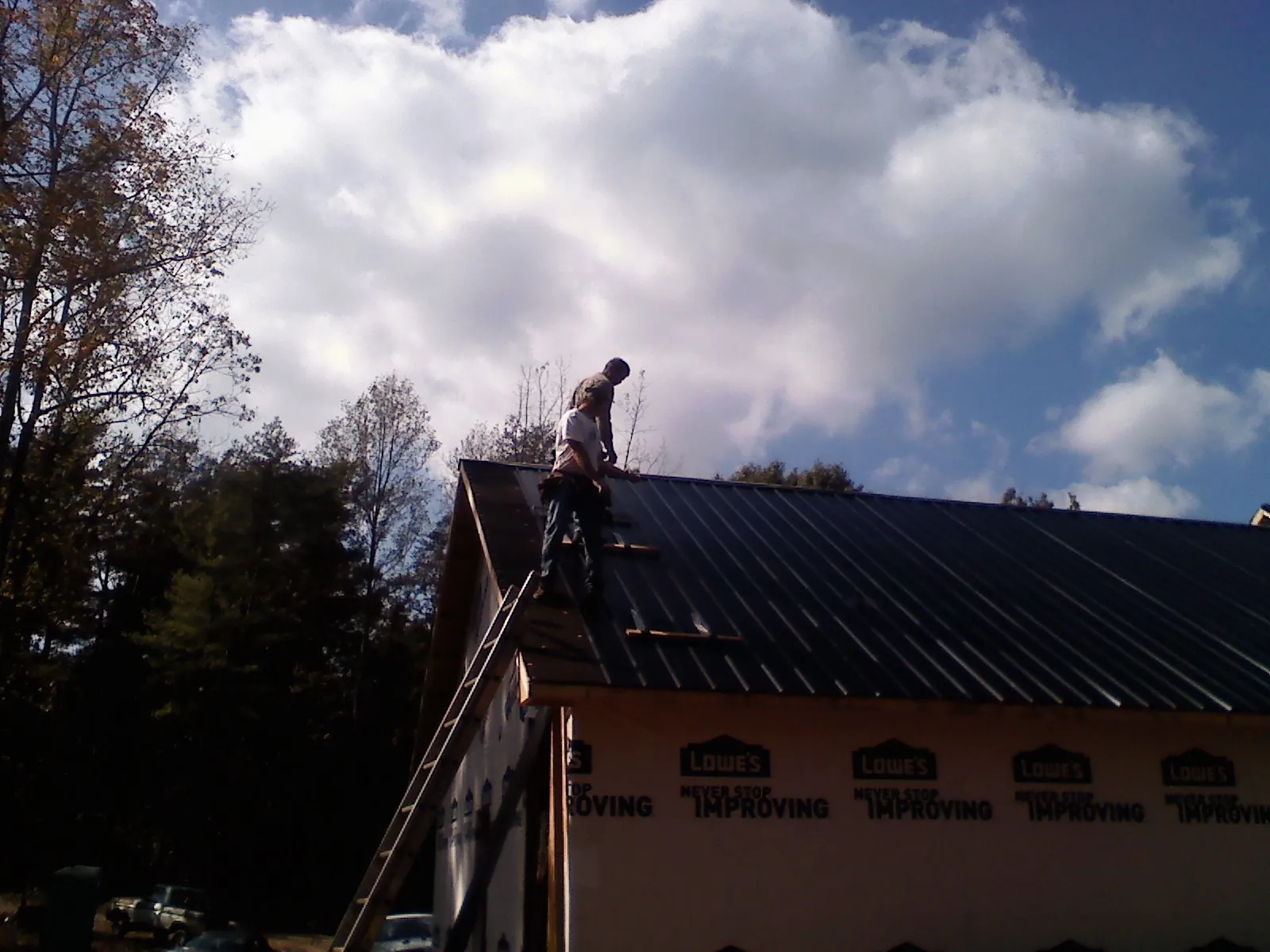 Roofer fastening dark metal panels high against a cloudy sky, from a Roof Inspection job in Versailles