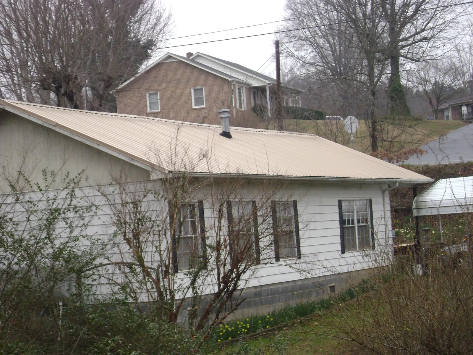 Tan metal roof on a white sided house set into a hillside — Commercial Roofing by Roofing Brothers in Versailles