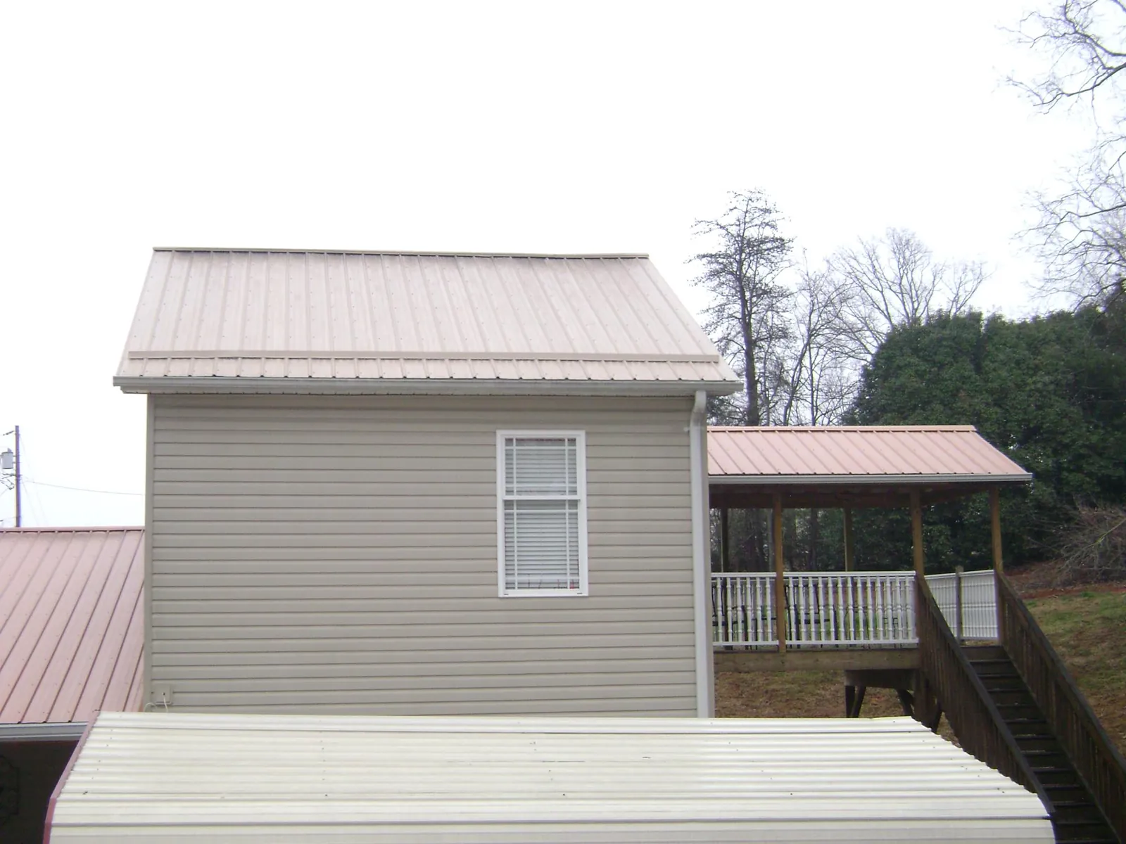 Tan metal roofs on a two story addition and attached porch, from a Roof Replacement job in Versailles